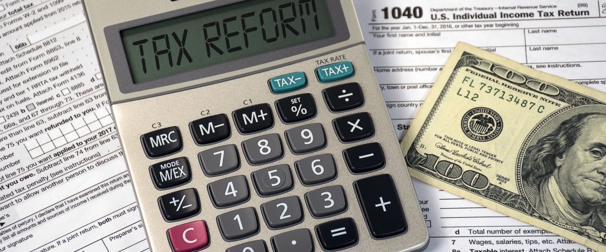 tax reform text on calculator screen with hundred dollar bill on 1040 income tax form