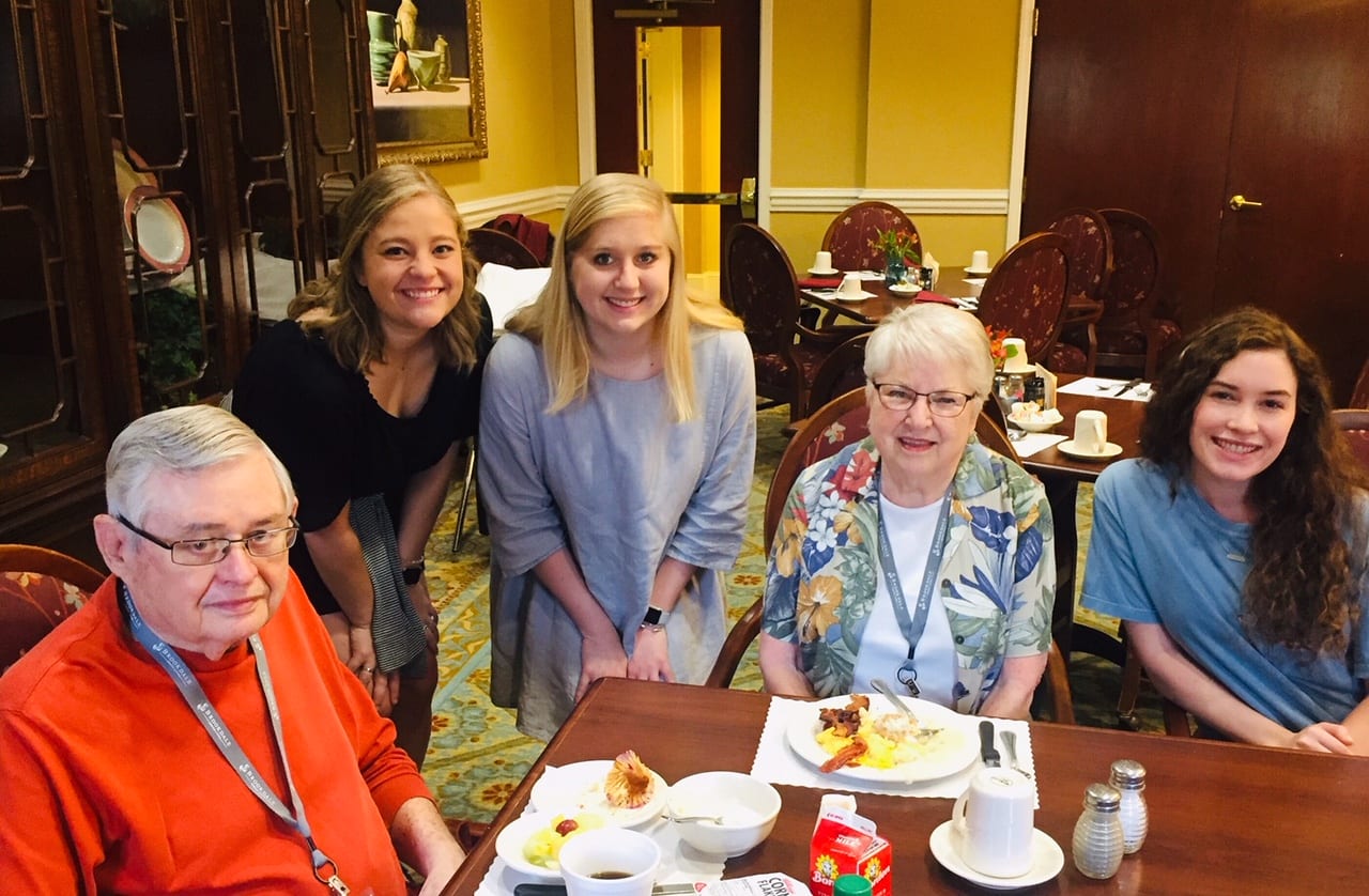 Senior Scene Brookdale 2 female students standing next to table with residents