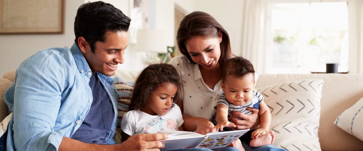 Family of four on a couch reading a book together.