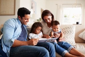 Family of four on a couch reading a book together.