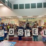Welcome back to class first priority kids holding gospel sign