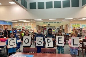 Welcome back to class first priority kids holding gospel sign